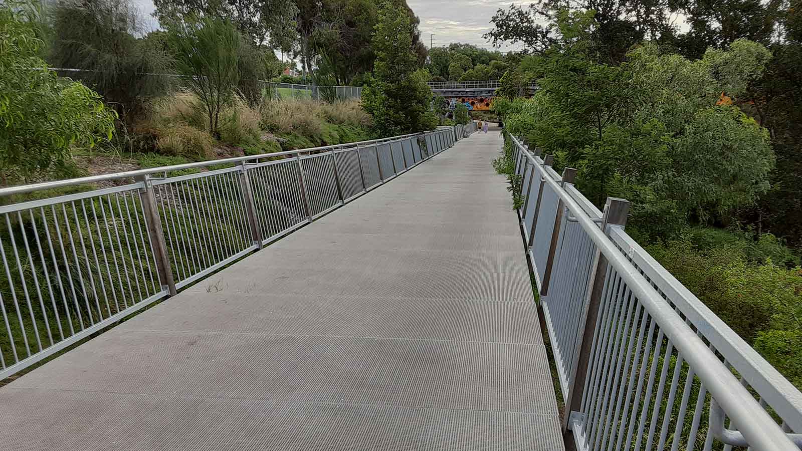 pedestrian bridge made from frp with steel railings spans small ravine.