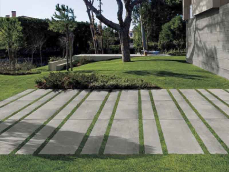 cement colored porcelain paver planks laid over gras in rows.