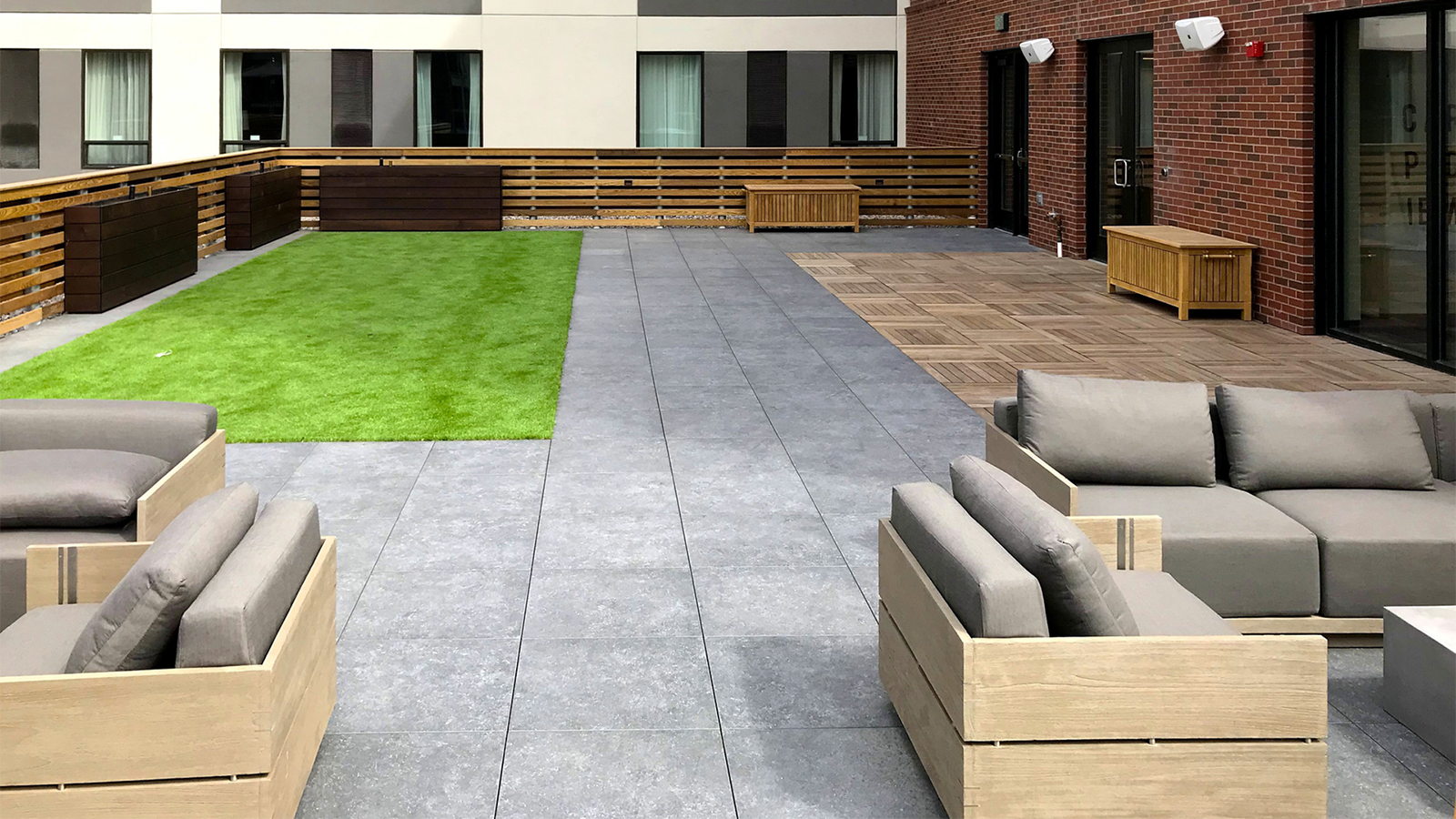 Roofdeck showing artificial turf, dark grey porcelain pavers, and ipe structual wood tiles on the right. patio couches in the right foreground. 