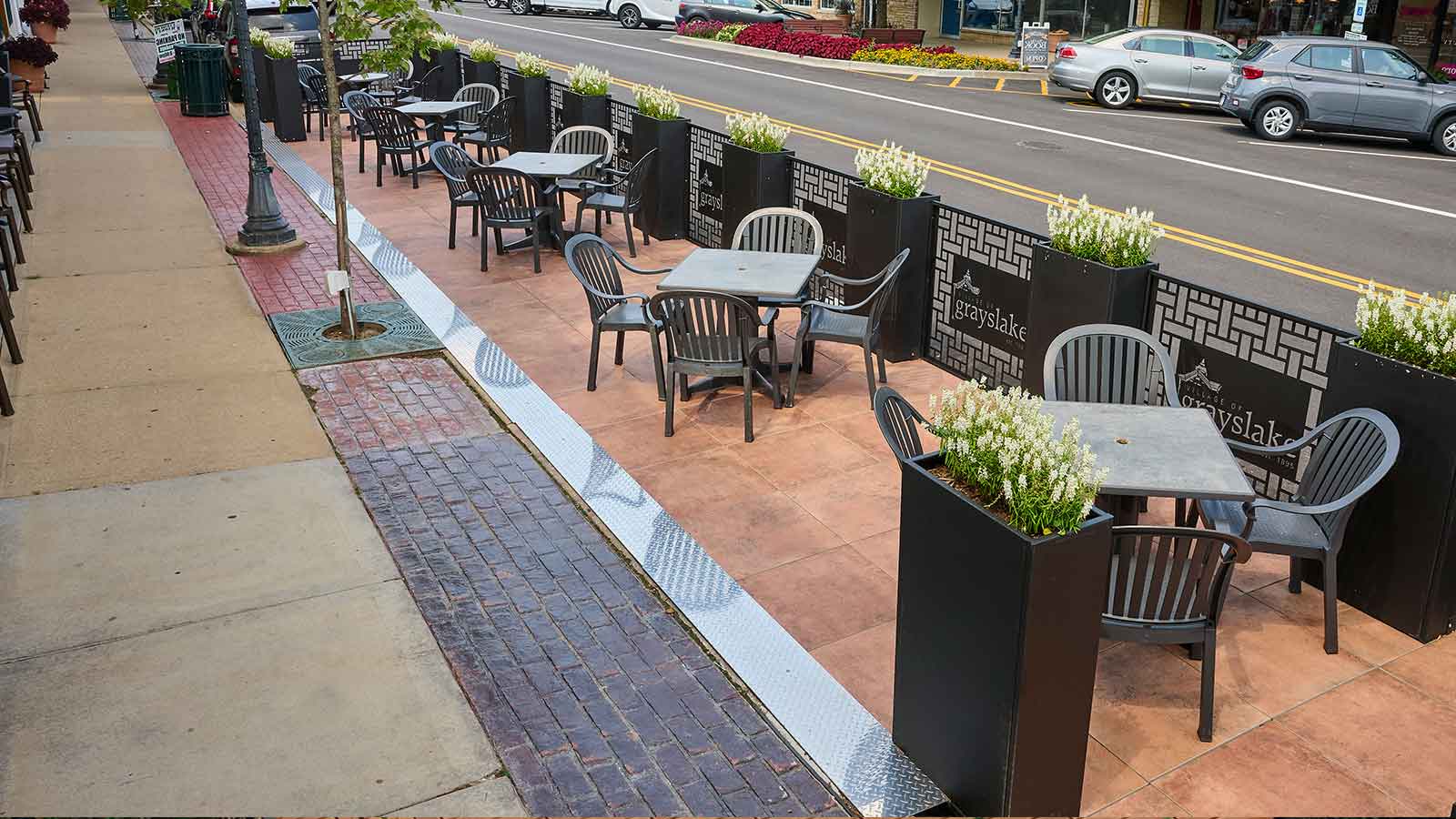 street dining parklet with tables, rustic pavers, and planters with white flowers.