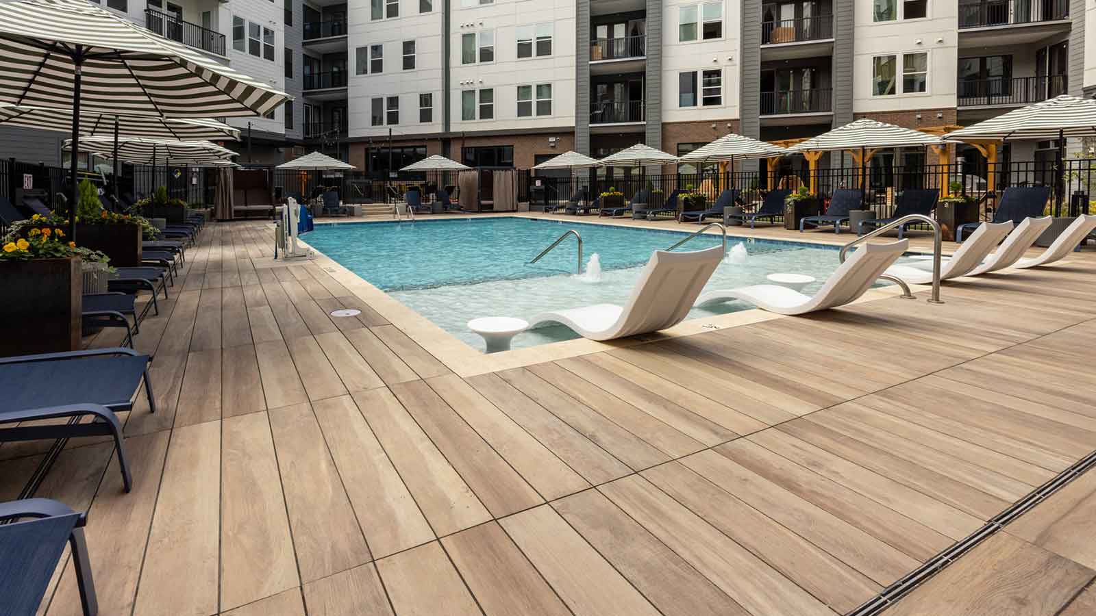 wood look porcelain planks around a pool with umbrellas and water lounge chairs.