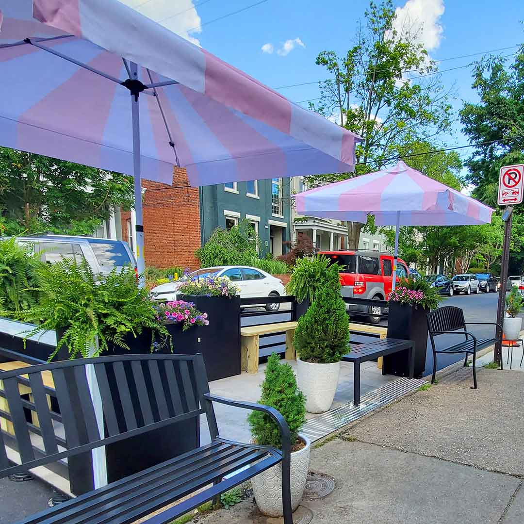 small parklet with 2 umbrellas and green shrubs and landscaping