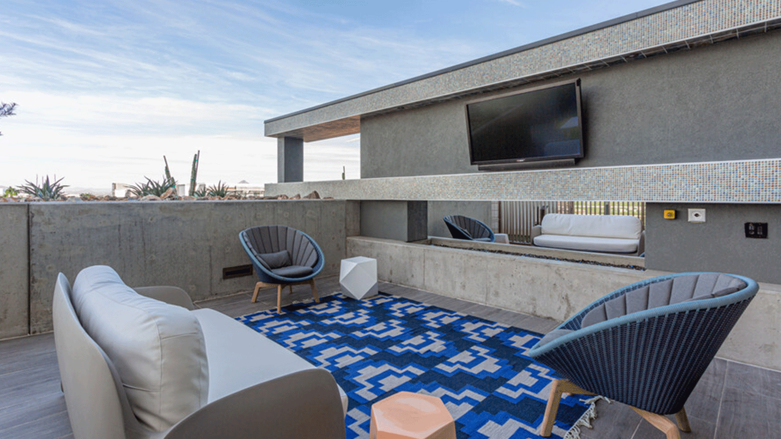 rooftop lounge area with couches, chairs, and blue rug. 