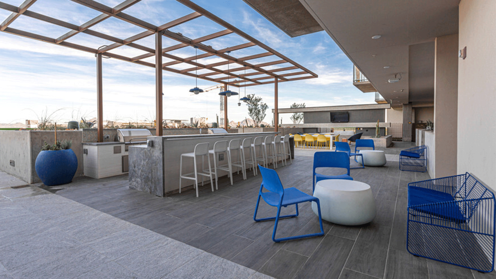 rooftop deck on a multifamily building with blue chairs, wood look pavers as surface, and deck kitchen area. 