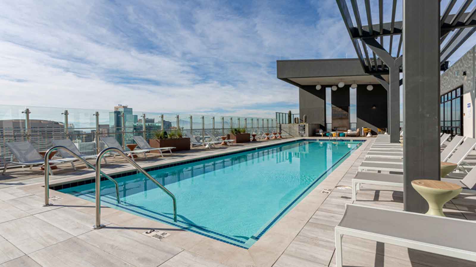 rooftop pool deck with city view, lounge chairs on the right, and light gray porcelain pavers around the pool.