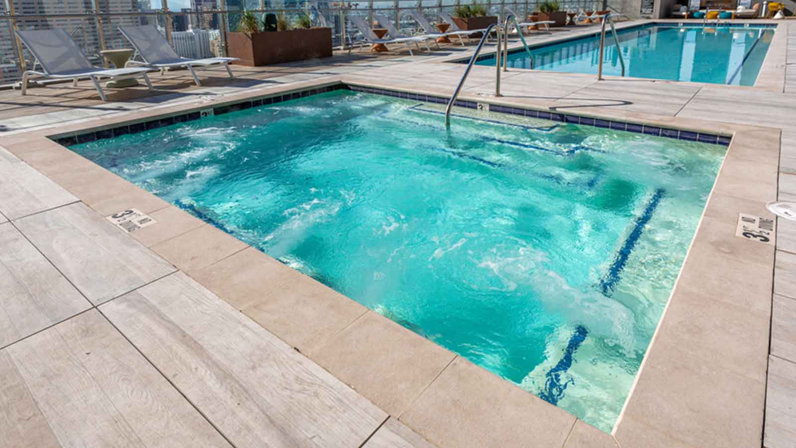 rooftop deck and pool area with a hot  tub and wood-look porcelain pavers surrounding pools. 