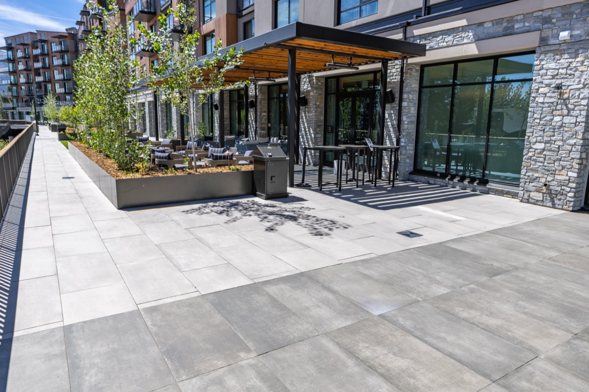 a patio terrace with two colors of gray and cream porcelain pavers as the surface, planters with trees and small shrubs along with pergola.