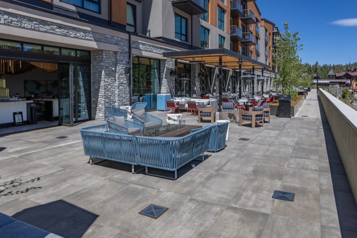 A hotel terrace with grey porcelain pavers as surfface with patio furniture in foreground and trees farther down the terrace.