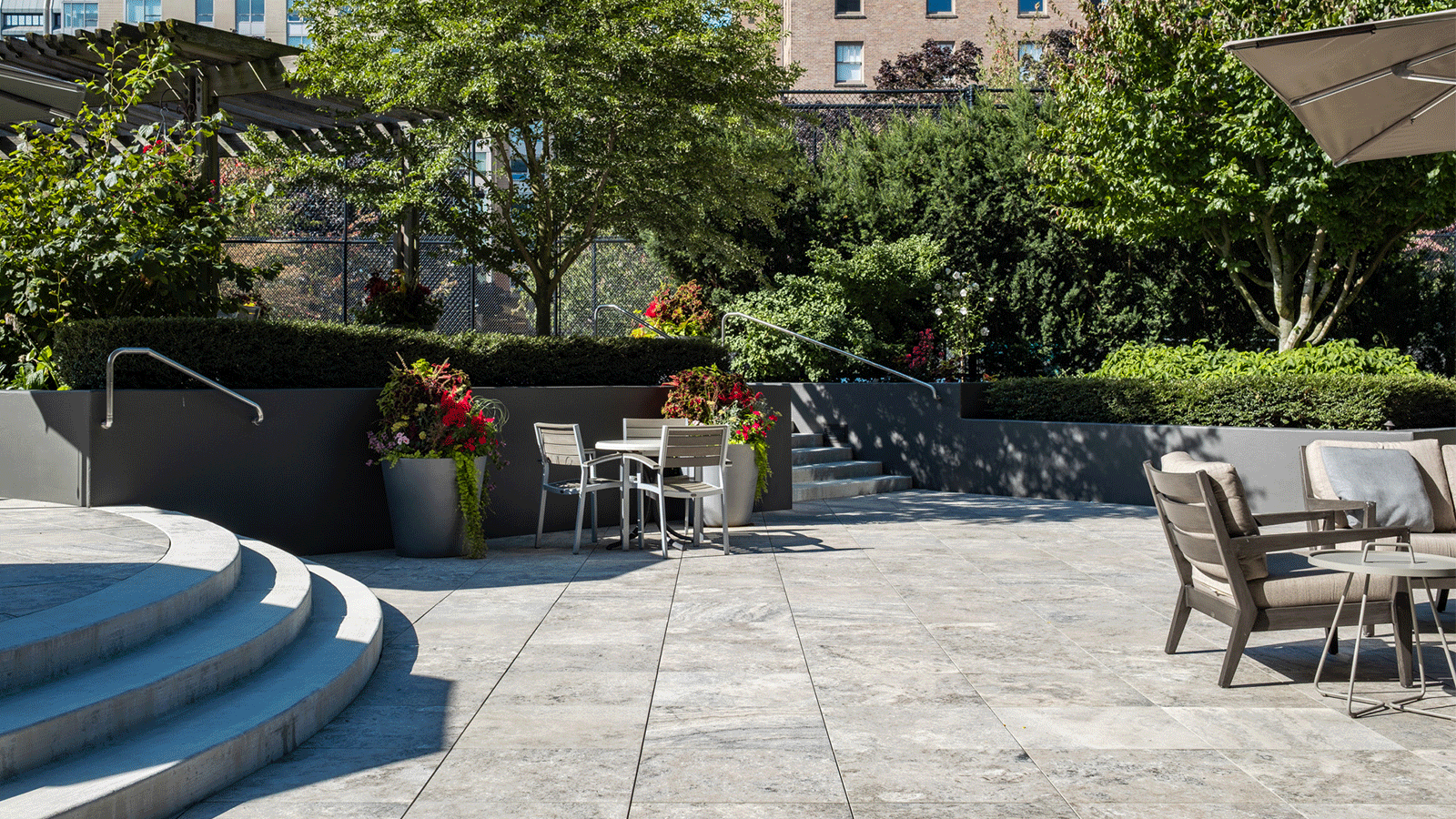 Patio in sunshine at plaza first hill in seattle, cement stairs on left, porcelain pavers in middle, paito furniture on right of image. 