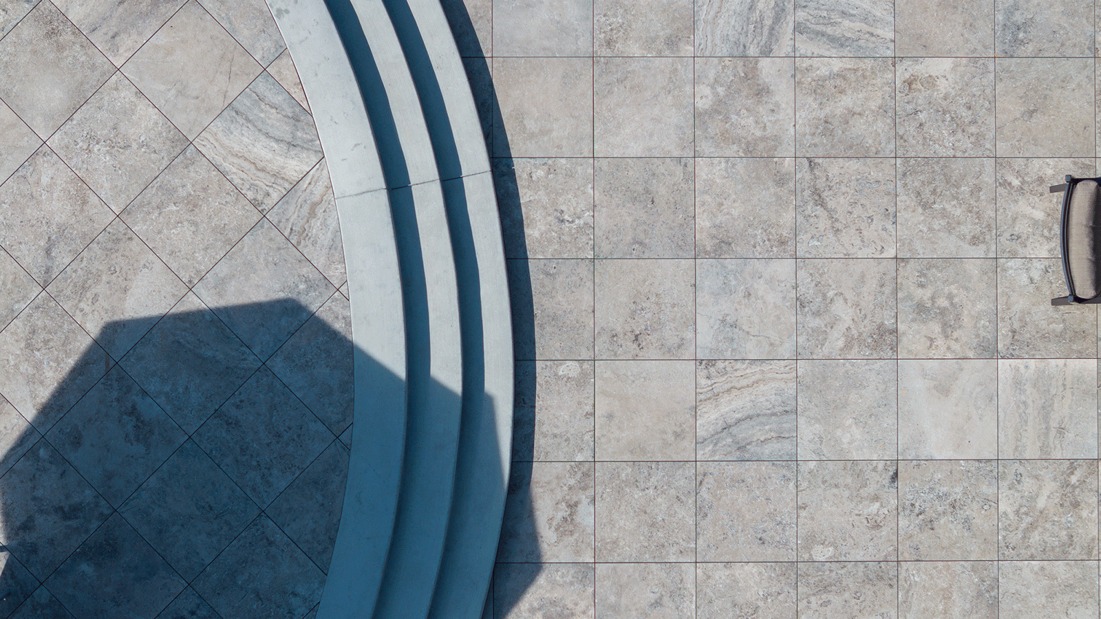 top down view of cream pavers with 3 curved cement stairs on left side of image.