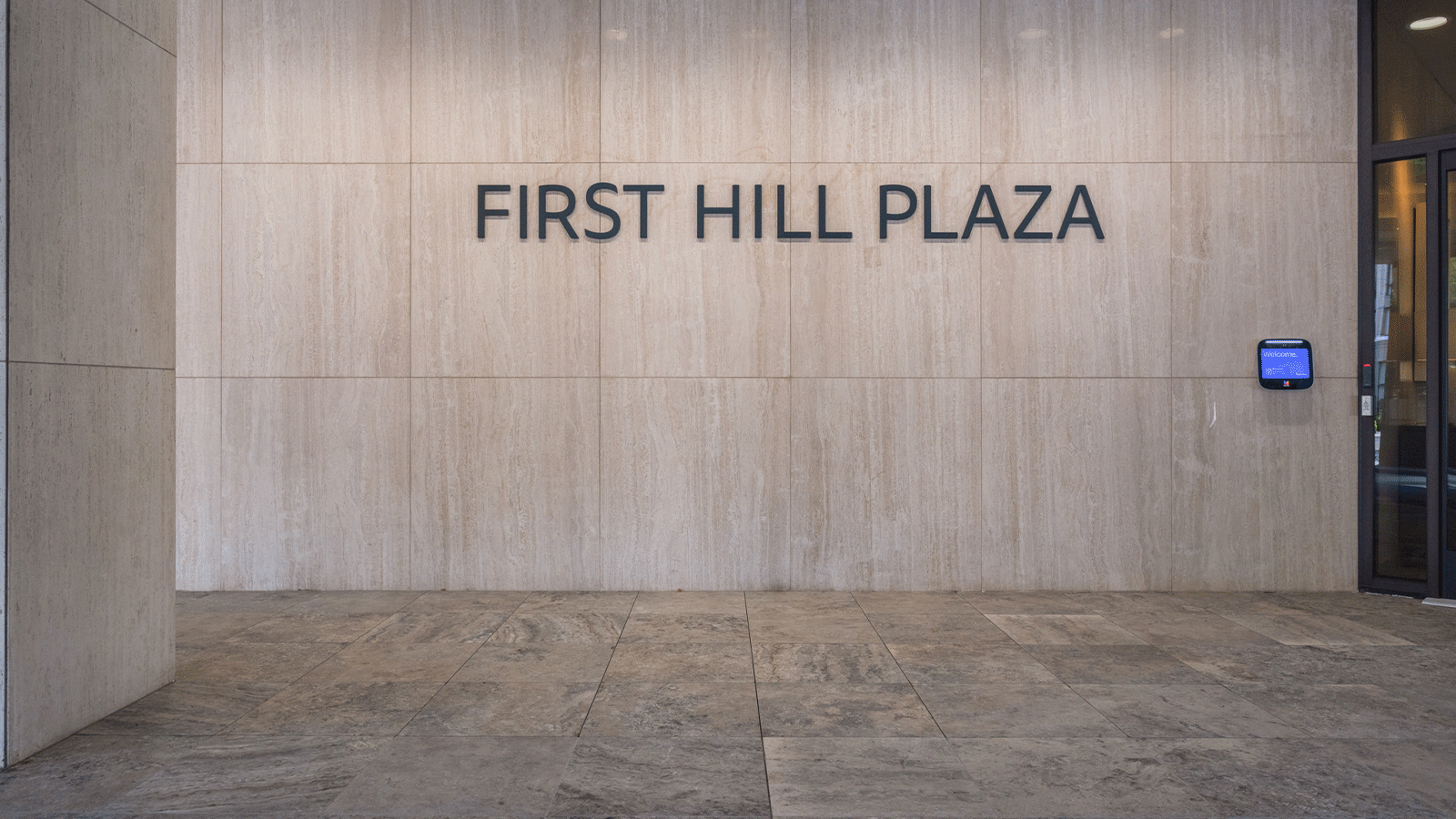 Entrance to first hill plaza, name on wall, brown and cream pavers in the foreground