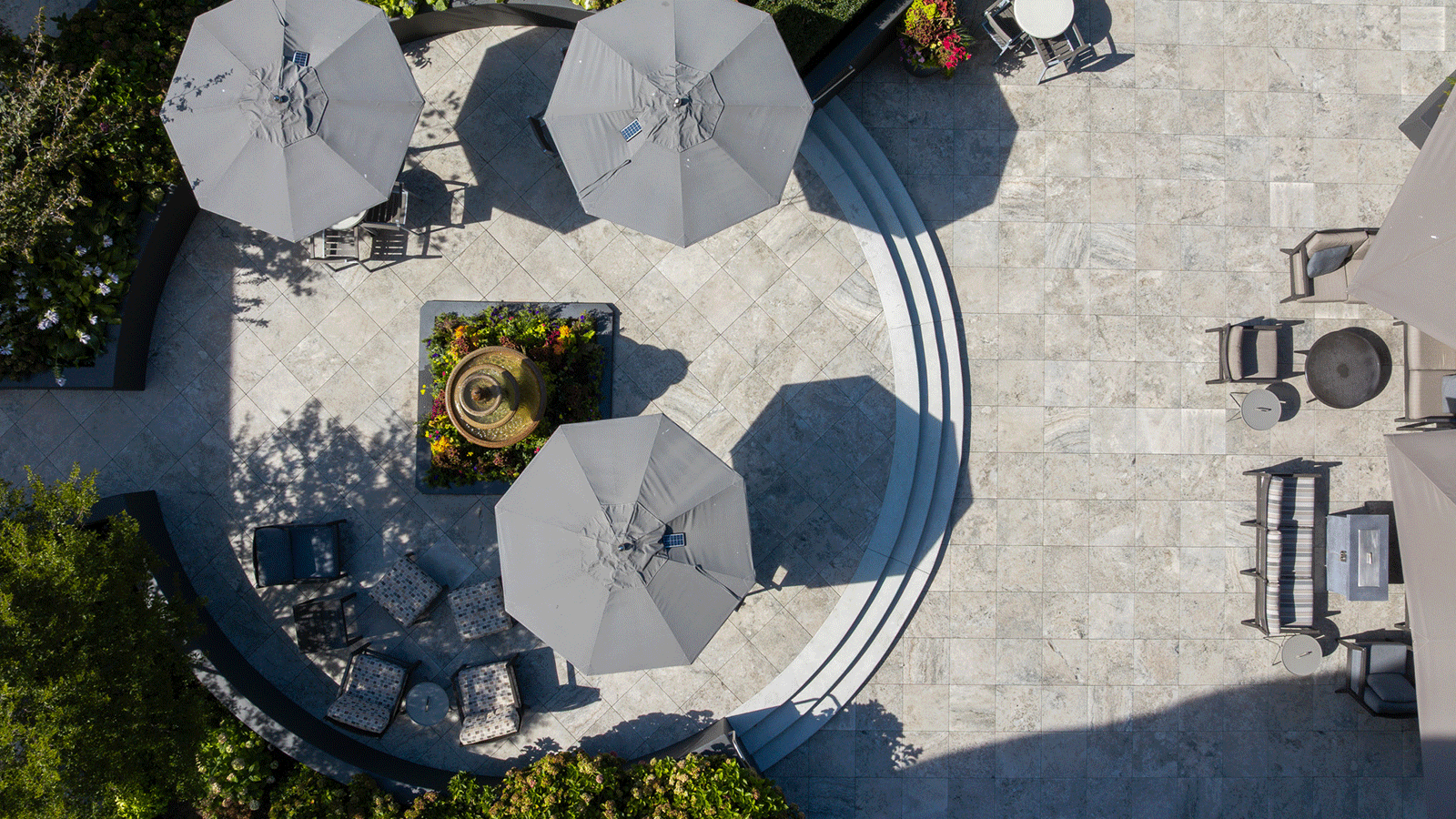 travertine porcelain pavers in cream cappuccino pattern from a birds eye top down view with shade umbrellas and green landscaping
