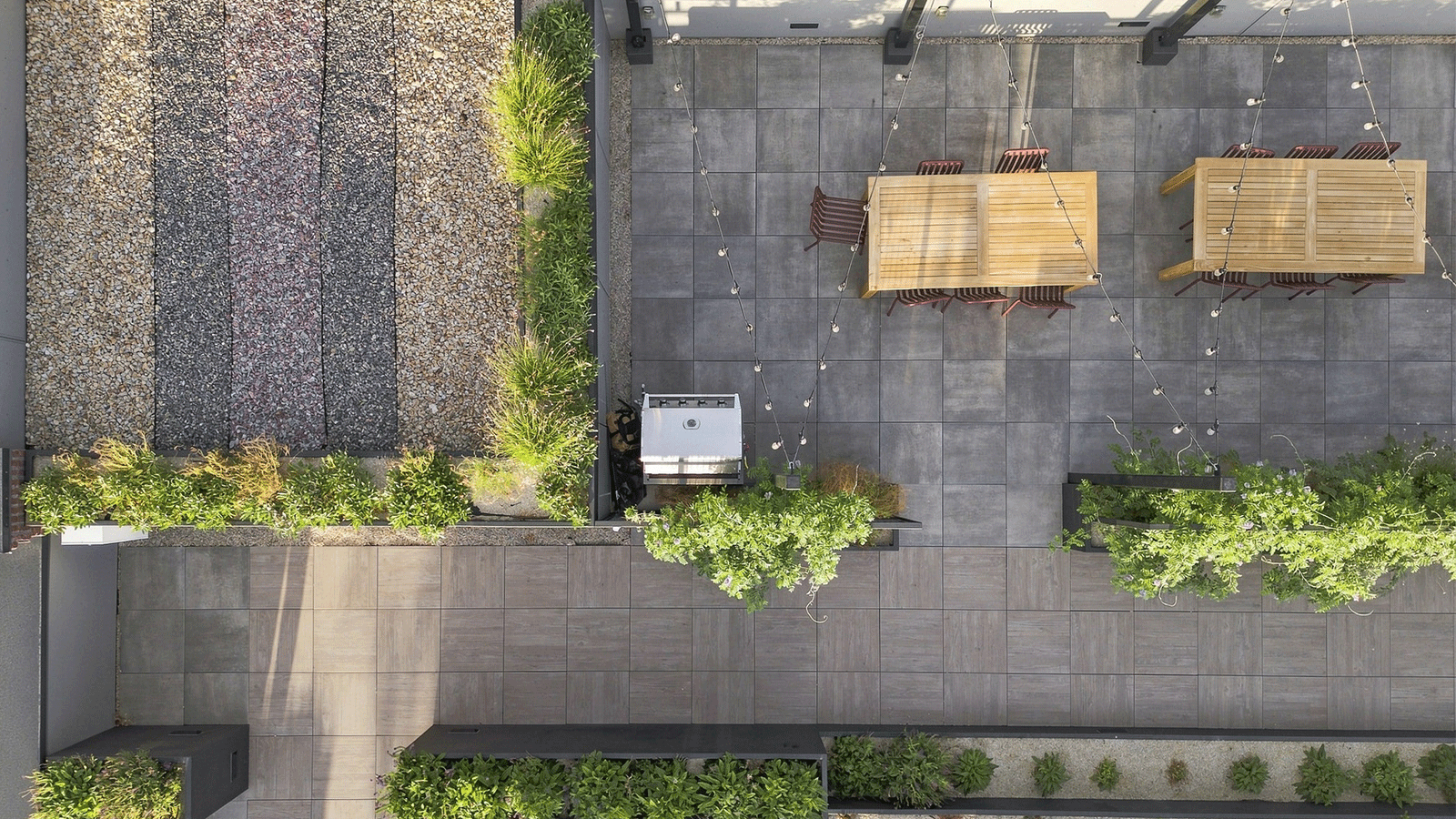 top down view of roof top deck with gray porcelain pavers, green landscaping planters, chairs and tables.