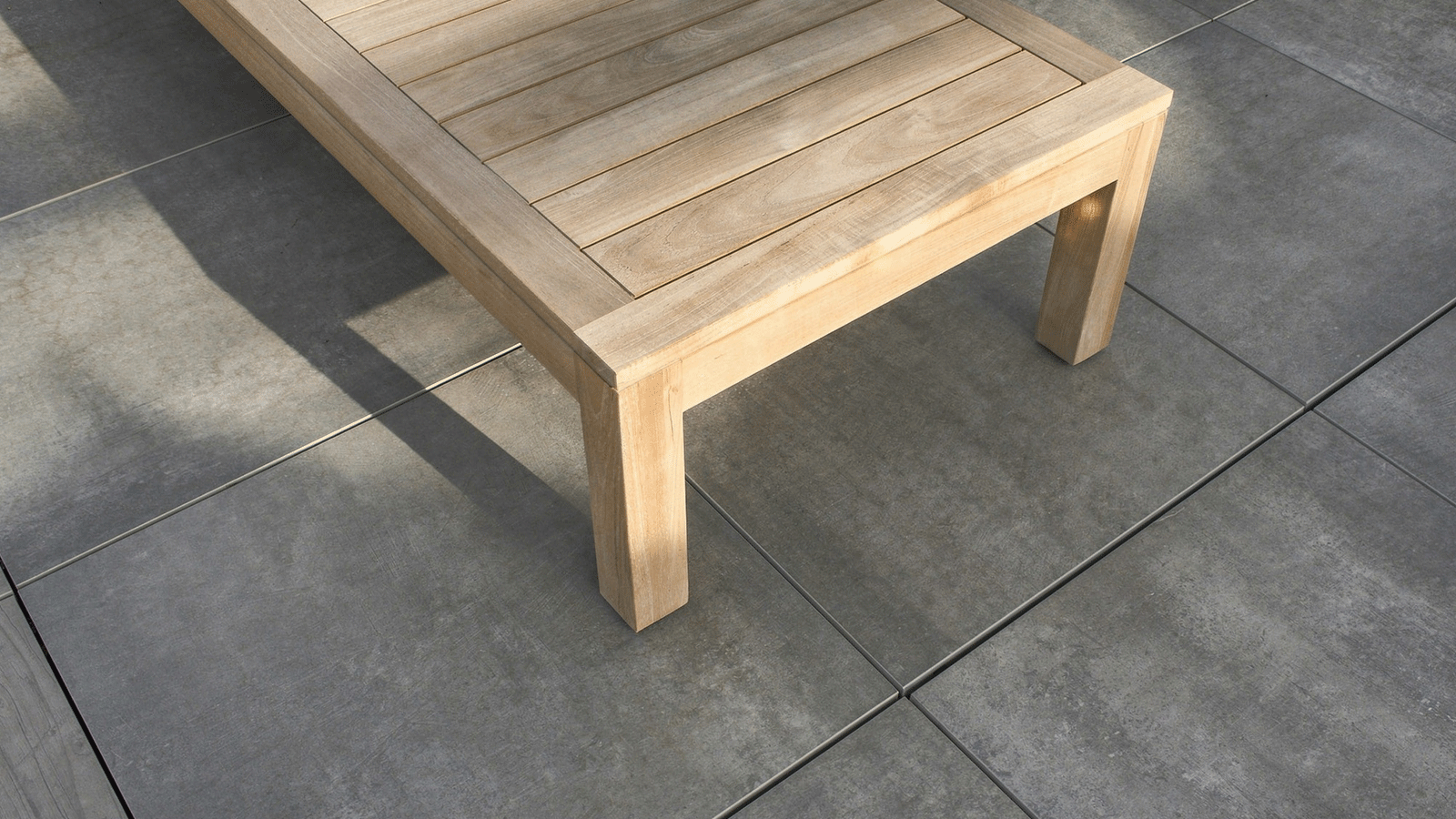 details view of gray sandalo porcelain pavers beneath a wood coffee table on a roof deck.