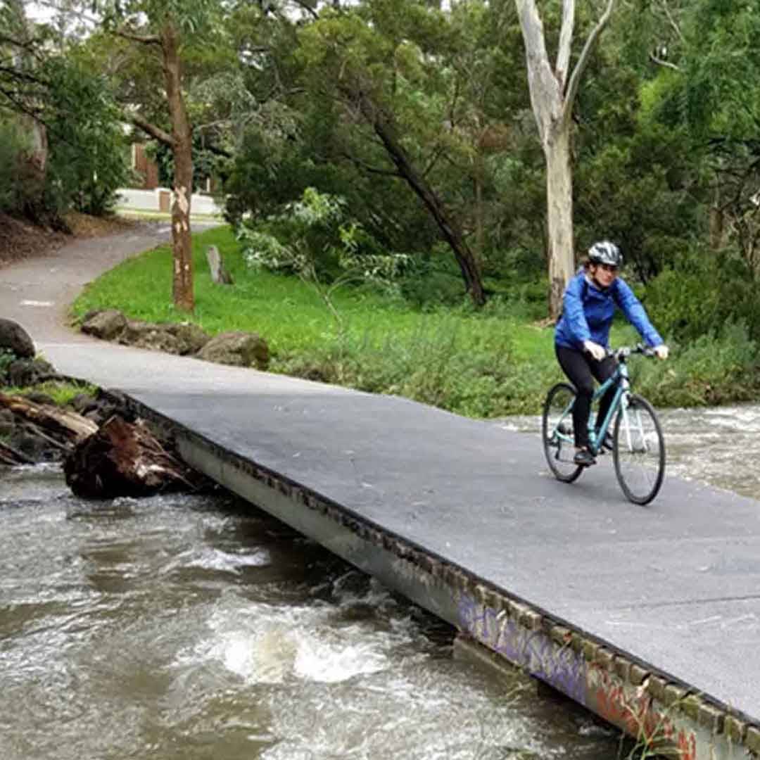 woman riding bike over frp bridge with rushing water beneath